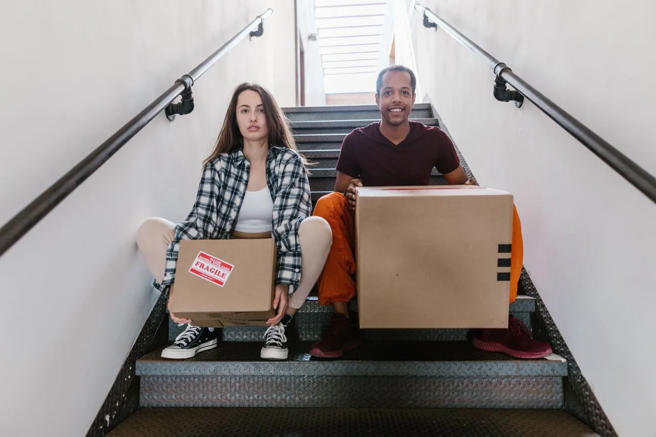 our-journey-02 Interracial couple sitting on stairs with cardboard boxes, ready for moving.
